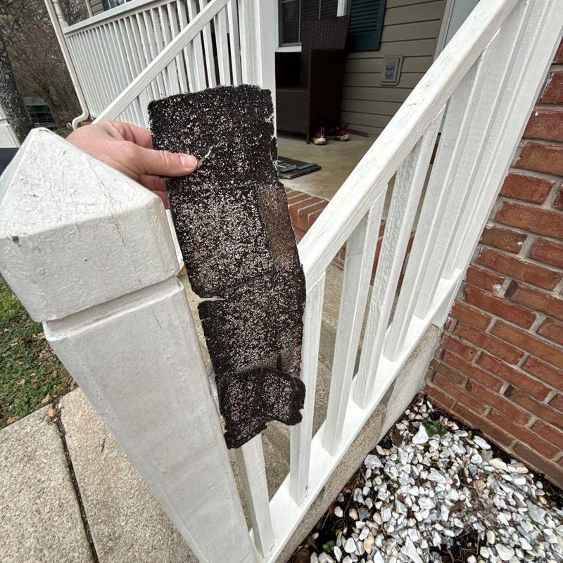 Asphalt roofing shingle with hail damage held by hand