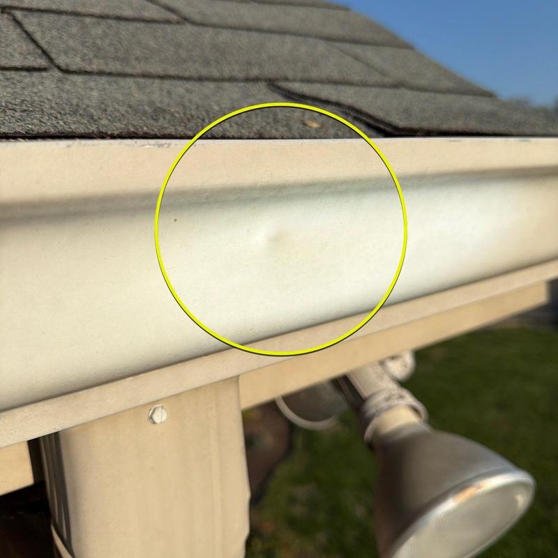 Gutter dent with yellow circle marking impact damage