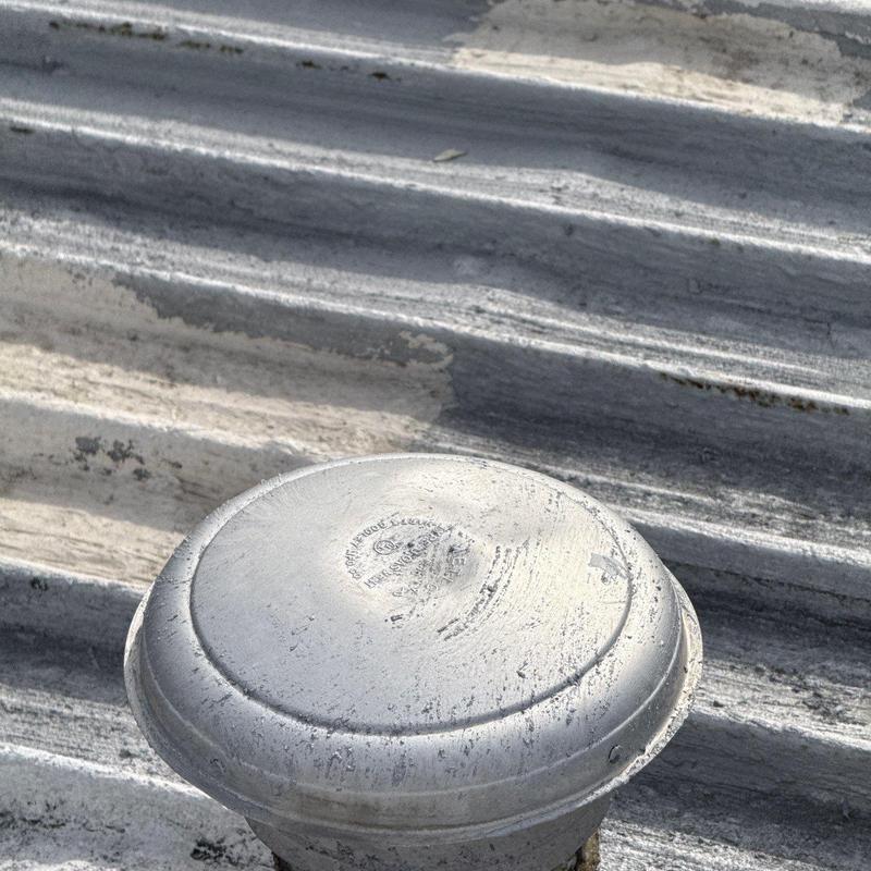 Metal roof vent with weathered hail damage on corrugated panels