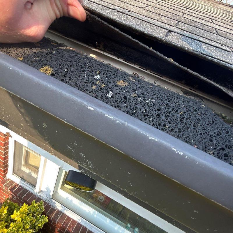 Roof shingles lifted to show gutter guard installation