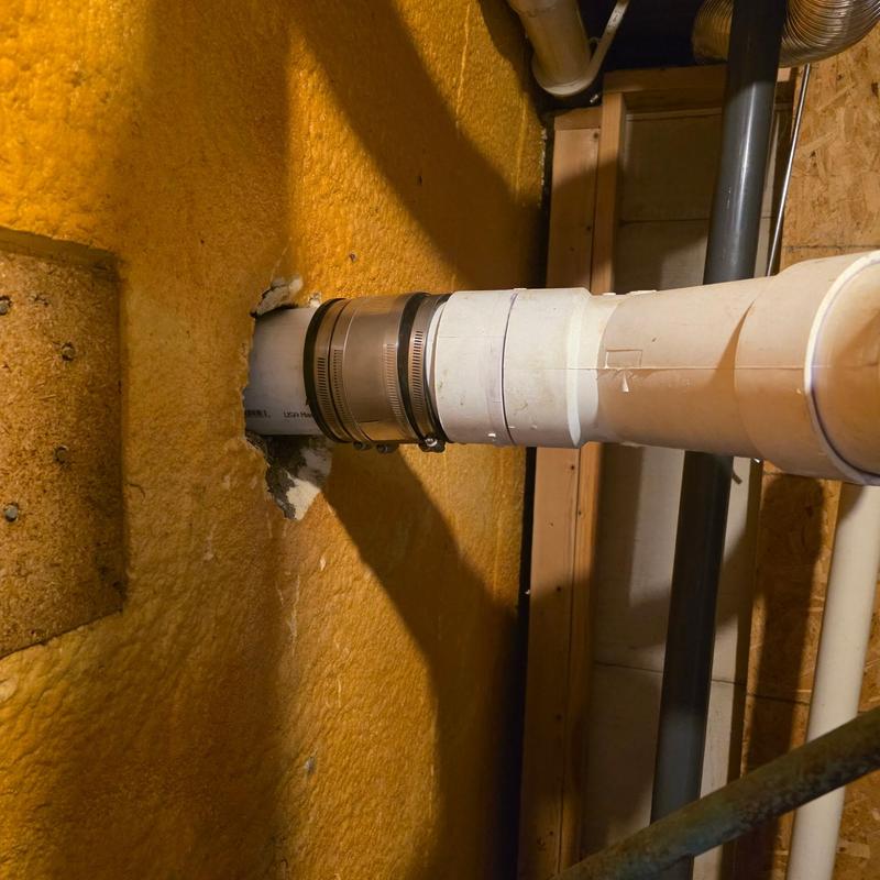 Septic line pipe connection with metal clamps in basement wall
