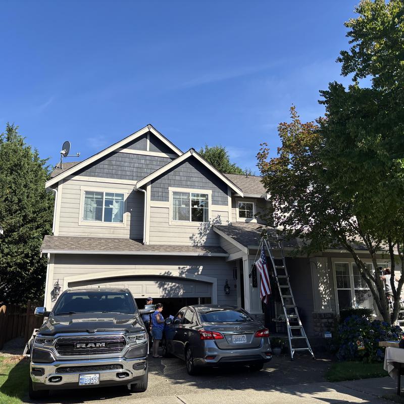 Asphalt shingle roof with ladder and vehicles in driveway