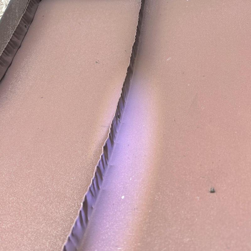 Metal roof panel edge with hail damage dents