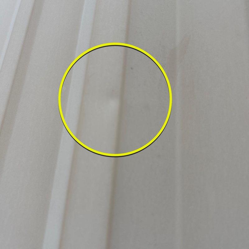 Metal roof panel with hail damage circled in yellow