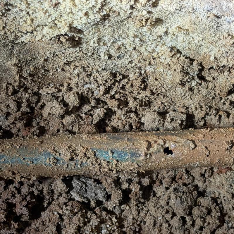 Copper water pipe with leak hole in soil under slab