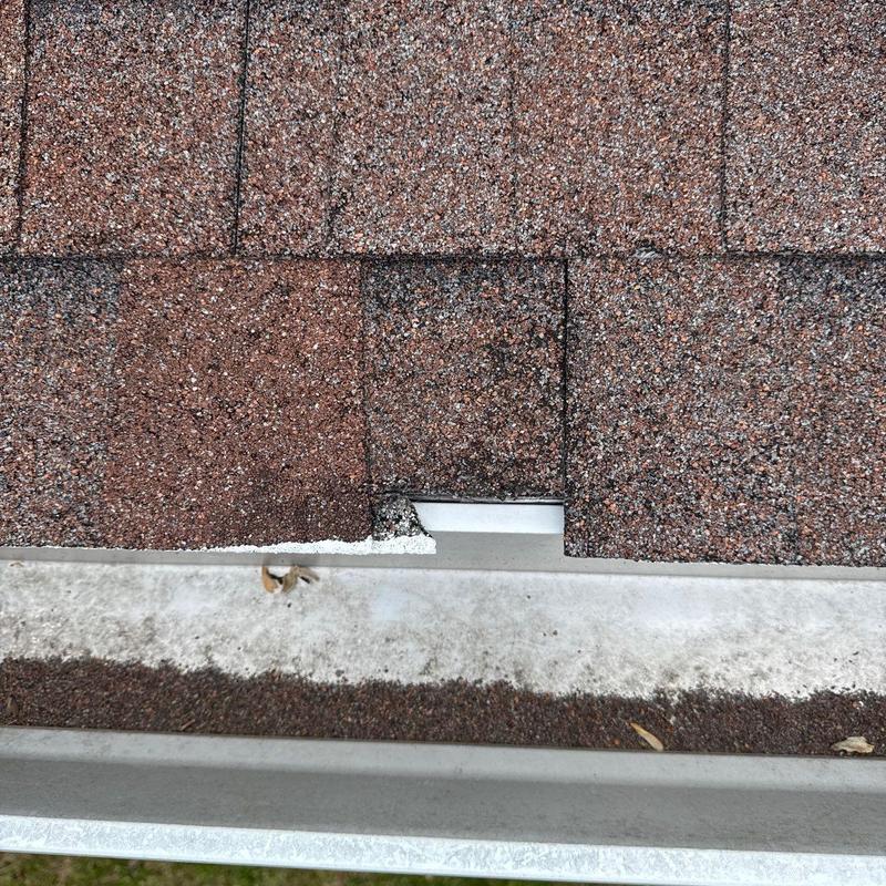 Asphalt shingles with visible hail damage near gutter edge