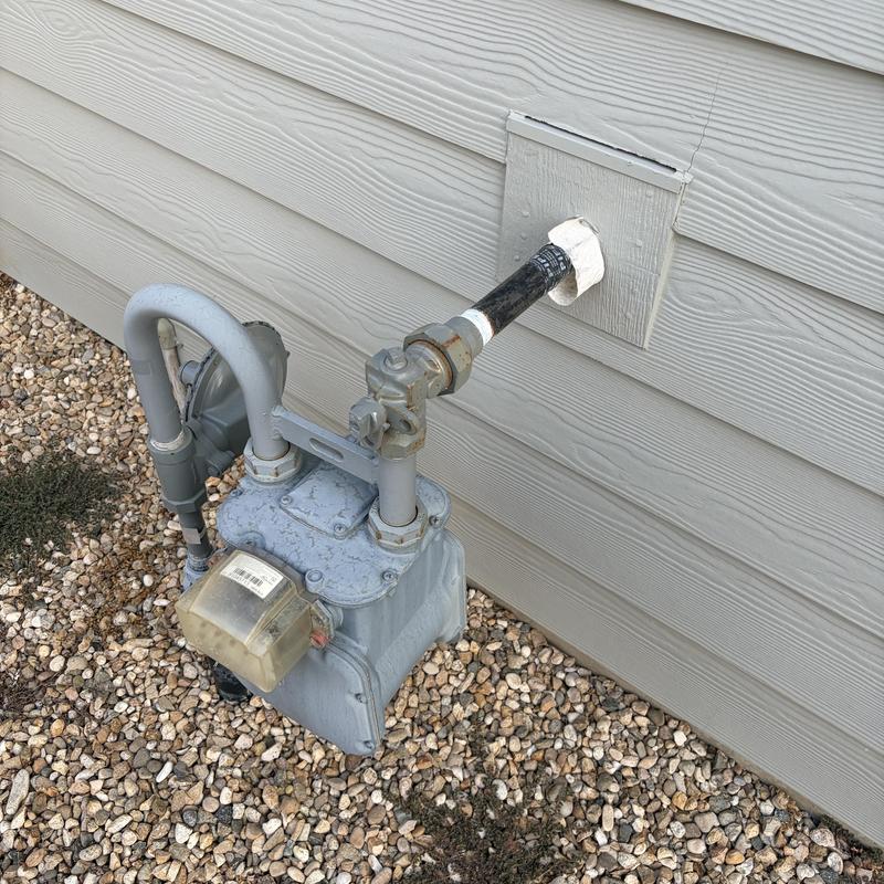 Exterior gas meter and piping installation by house wall