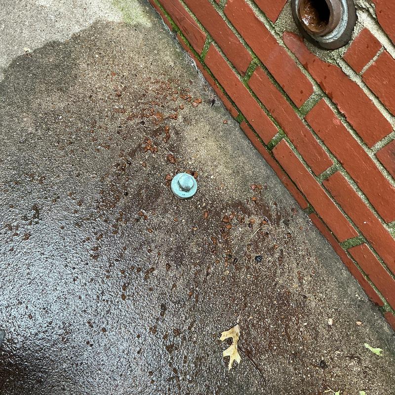 Kitchen drain cleanout cap on concrete near brick wall
