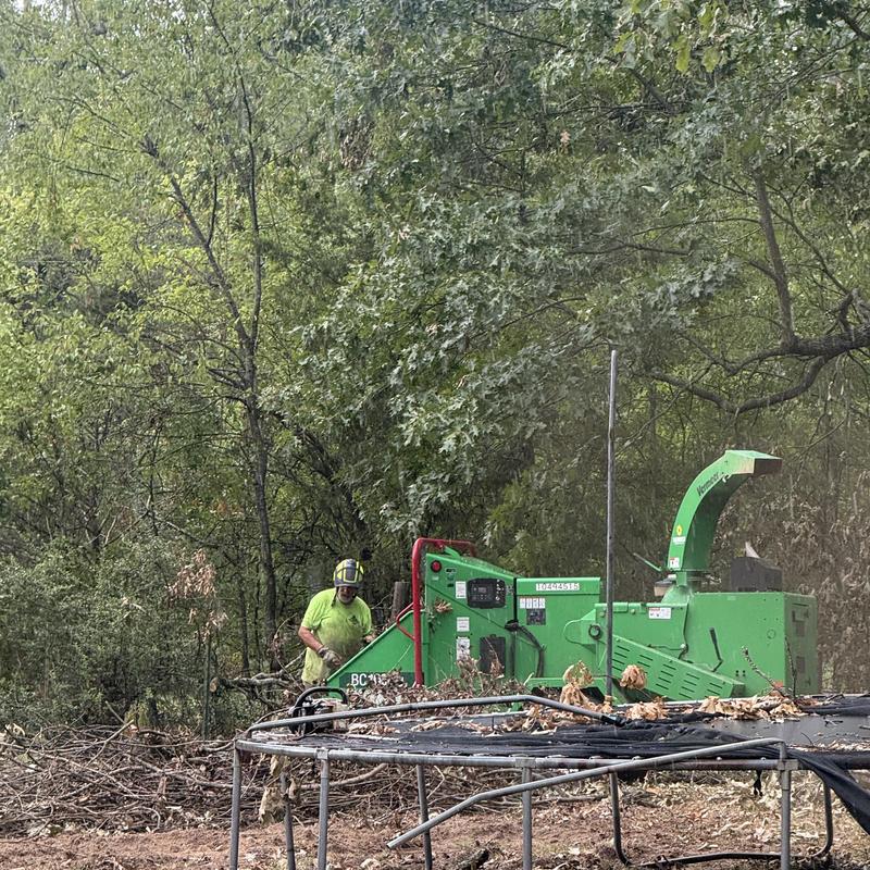 Wood chipper and debris clearing near trampoline