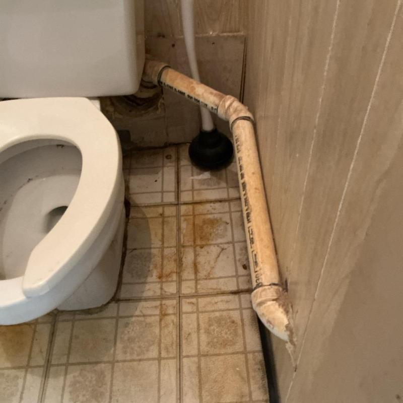 Toilet drain pipe with aged flooring and wall stains Toilet drain pipe with aged flooring and wall stains