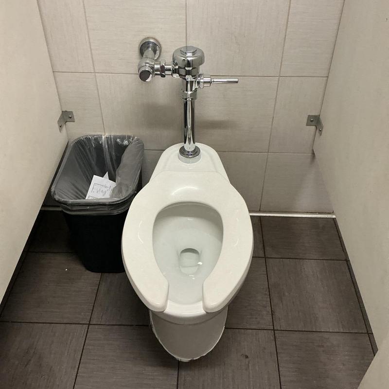 Toilet with chrome flushometer in warehouse bathroom stall Toilet with chrome flushometer in warehouse bathroom stall