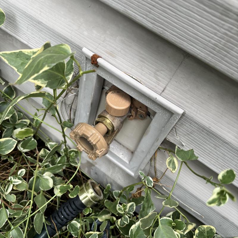Hose bib outside home with garden hose attached Hose bib outside home with garden hose attached