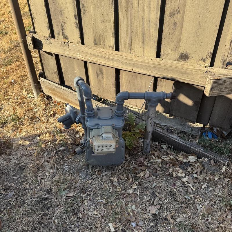 Natural gas meter and piping by wooden fence Natural gas meter and piping by wooden fence