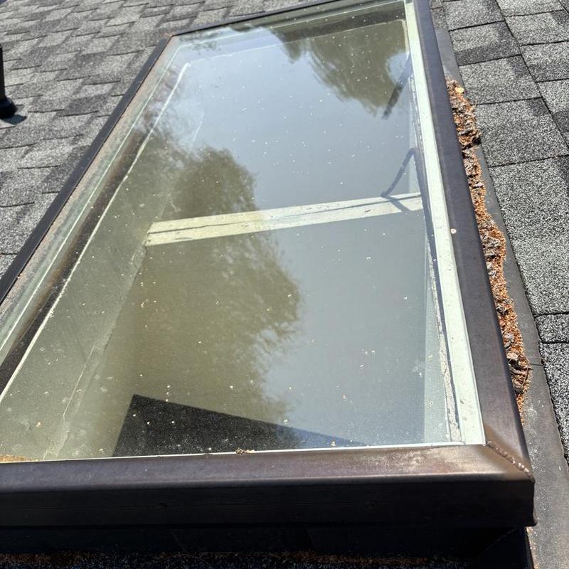 Skylight frame and flashing with roof debris buildup
