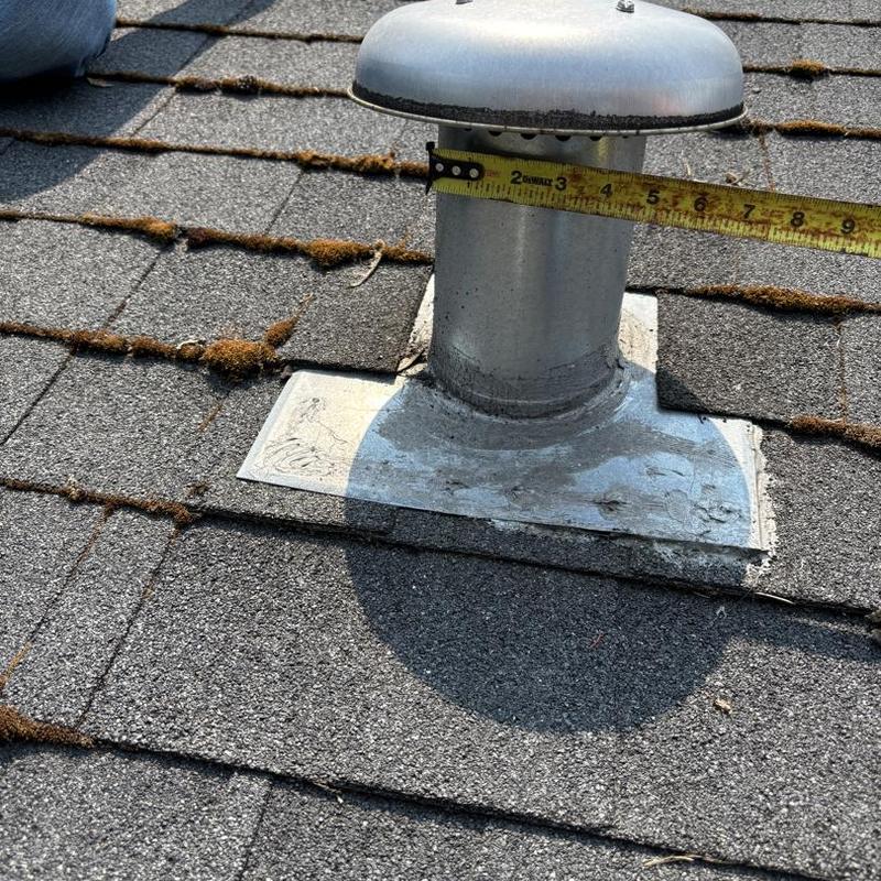 Roof vent flashing with measuring tape on shingle roof