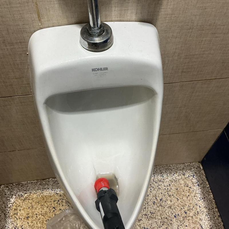 Urinal drain with auger clearing blockage in restroom