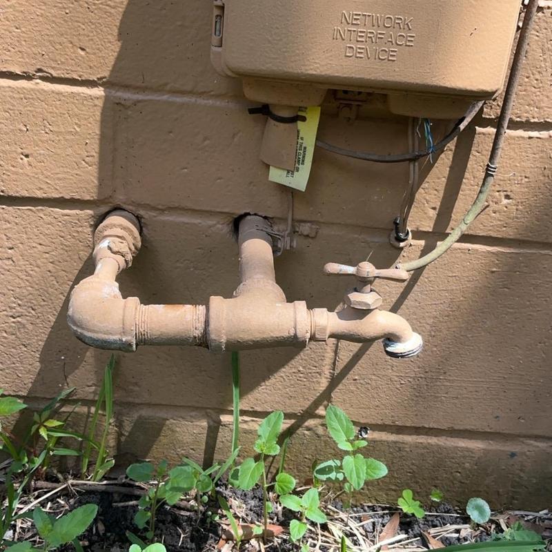 Galvanized outdoor hose bibb assembly on brick wall