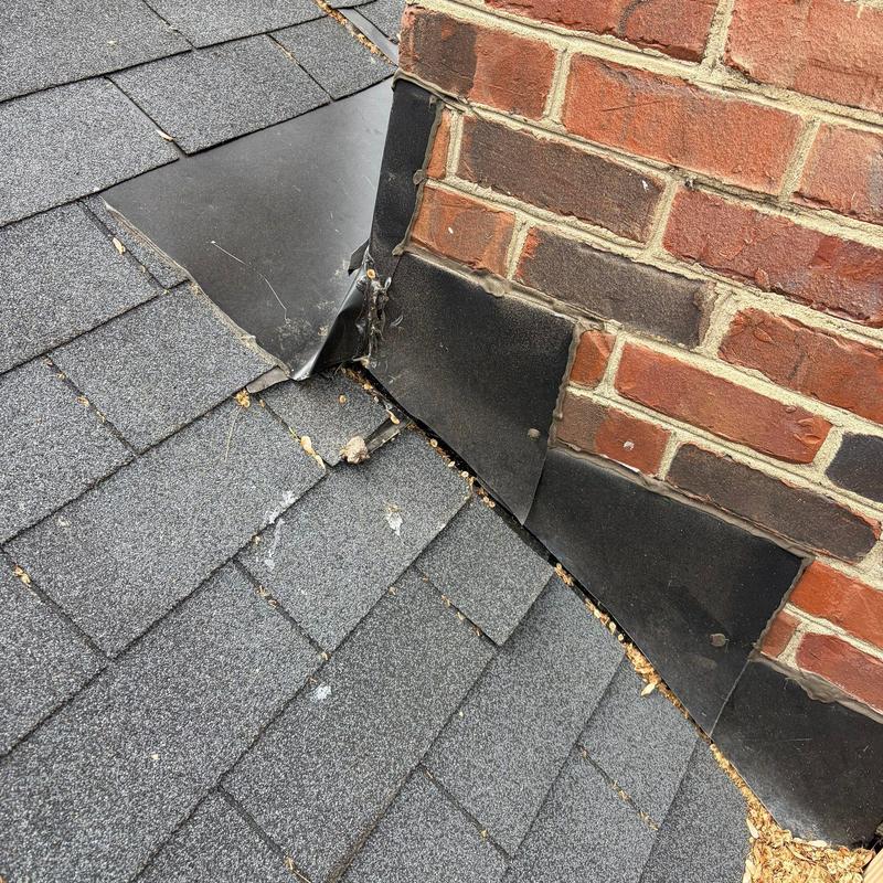 Roof flashing damage at brick chimney base on shingle roof