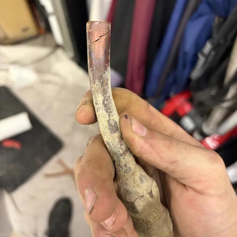 Cracked copper pipe showing leak damage in hand