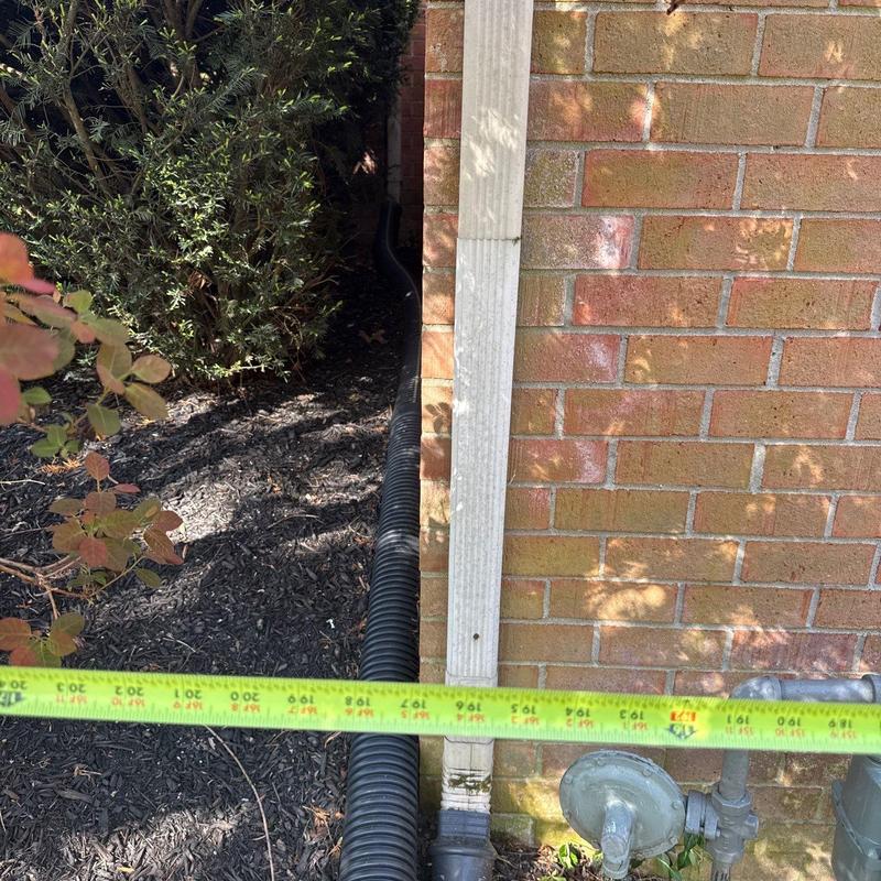 Downspout drainage pipe next to brick wall with tape measure