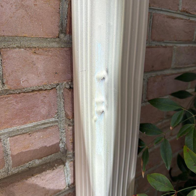 Downspout with dents and surface damage near brick wall