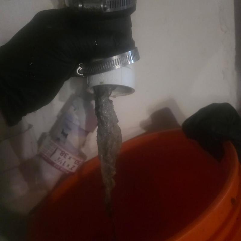 PVC pipe water flow into orange bucket with gloved hand