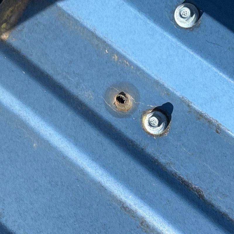 Metal roof panel with hail damage and loose bolt