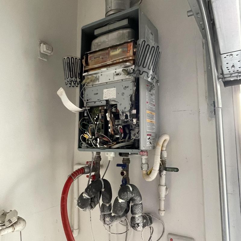 Tankless water heater with open panel and piping
