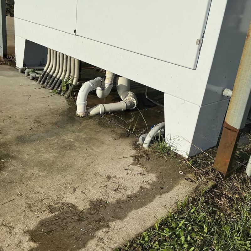 PVC drain pipes under HVAC unit with outdoor water leak