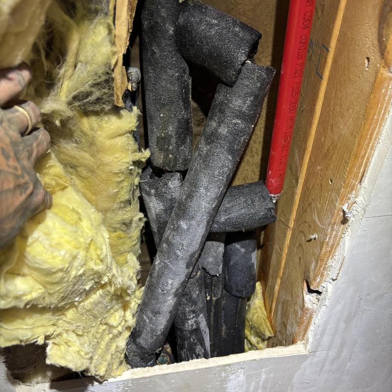 Insulated plumbing pipes inside wall cavity with damaged drywall