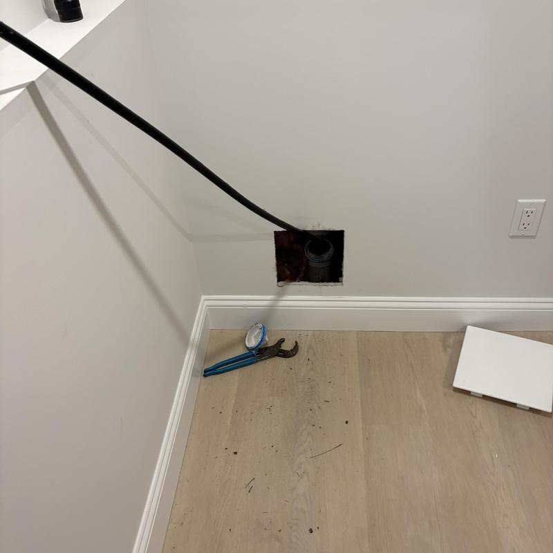 Drain pipe jetting hose in wall opening with wrench nearby Drain pipe jetting hose in wall opening with wrench nearby
