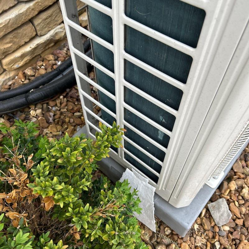 Air conditioner unit beside stone wall and bushes