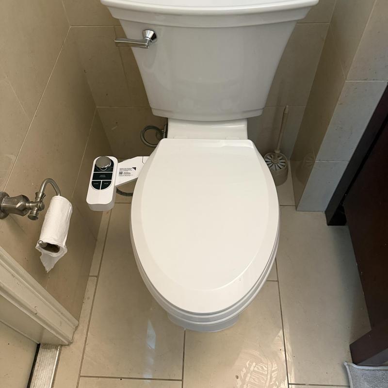 Toilet with bidet attachment installed in bathroom