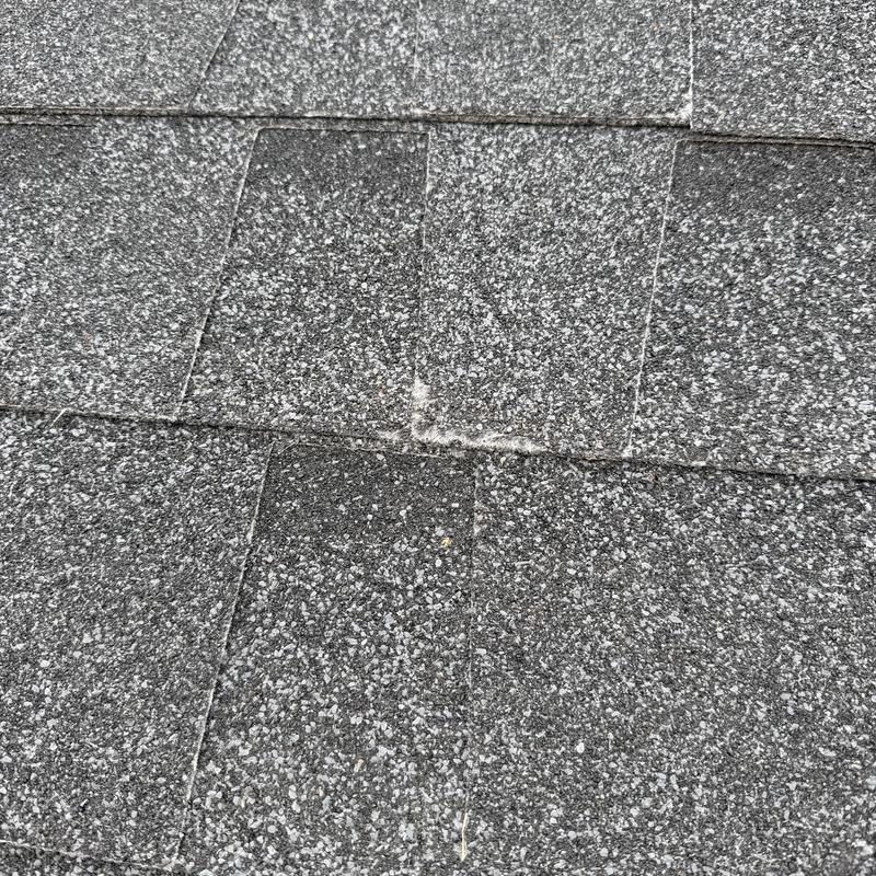 Asphalt shingle roof close-up showing damage spot Asphalt shingle roof close-up showing damage spot