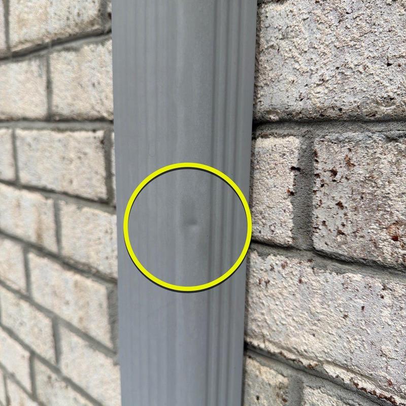 Downspout dent damage on exterior brick wall