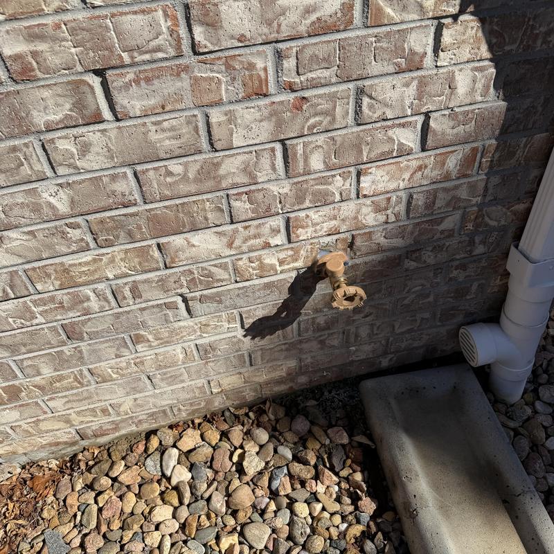 Hose bibb exterior faucet on brick wall with drainage pipe