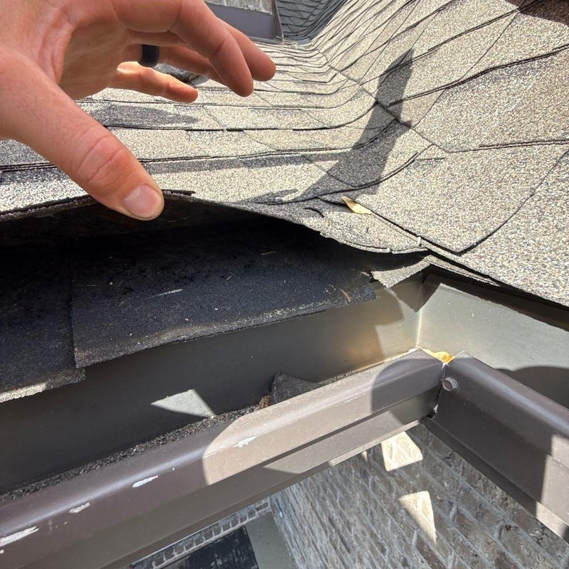 Roof shingles lifted revealing gutter and flashing underneath