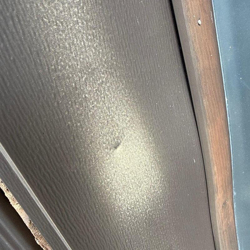 Metal siding hail damage close-up with wood trim nearby