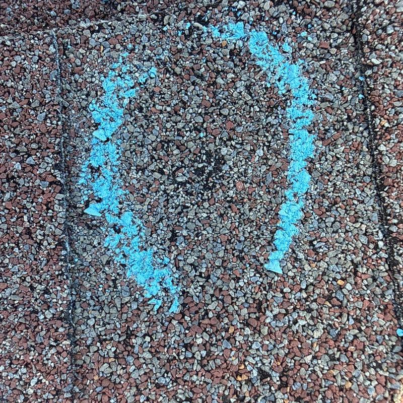 Roof shingles hail damage marked with blue chalk circle