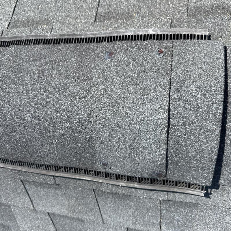 Roof ridge vent with lifted shingles and nail heads visible