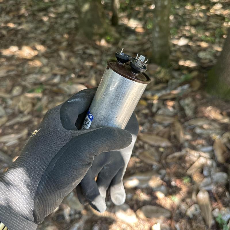 AC capacitor held by technician wearing gloves outdoors AC capacitor held by technician wearing gloves outdoors