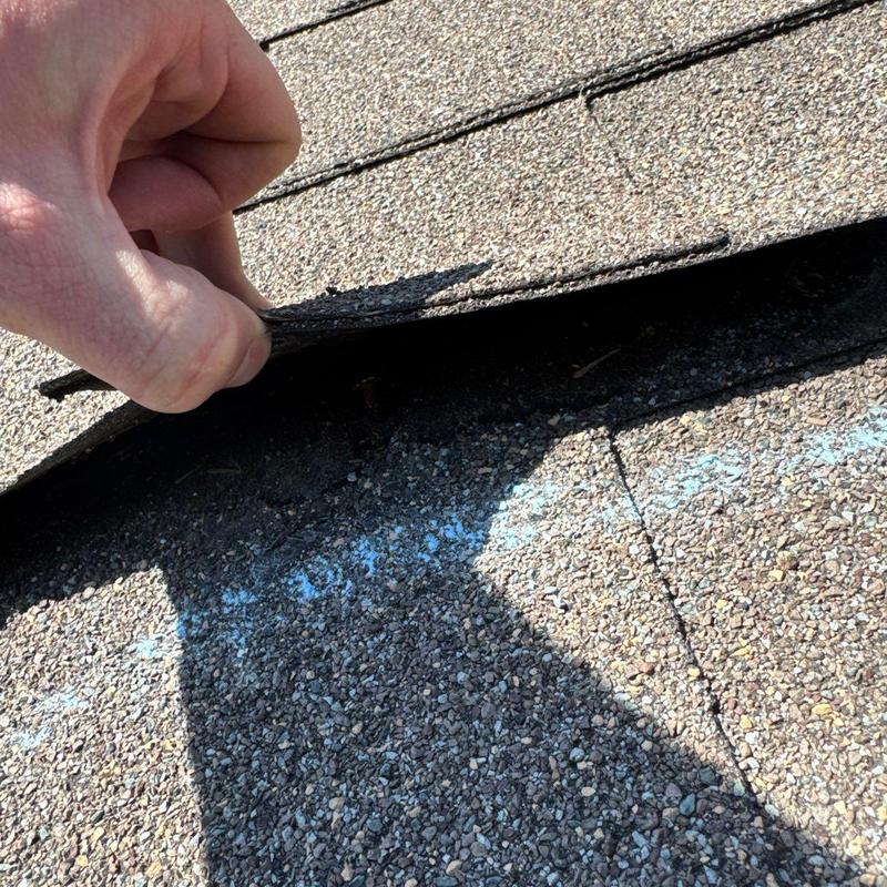 Asphalt roofing shingles lifted to reveal damage underneath