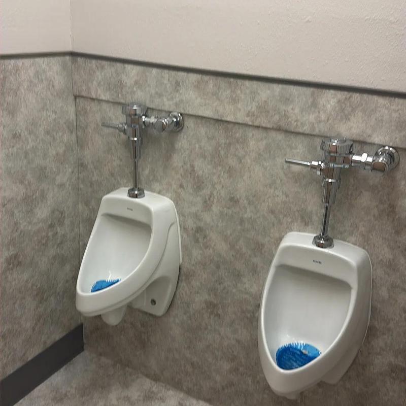 Urinal plumbing flush valves in restroom corner