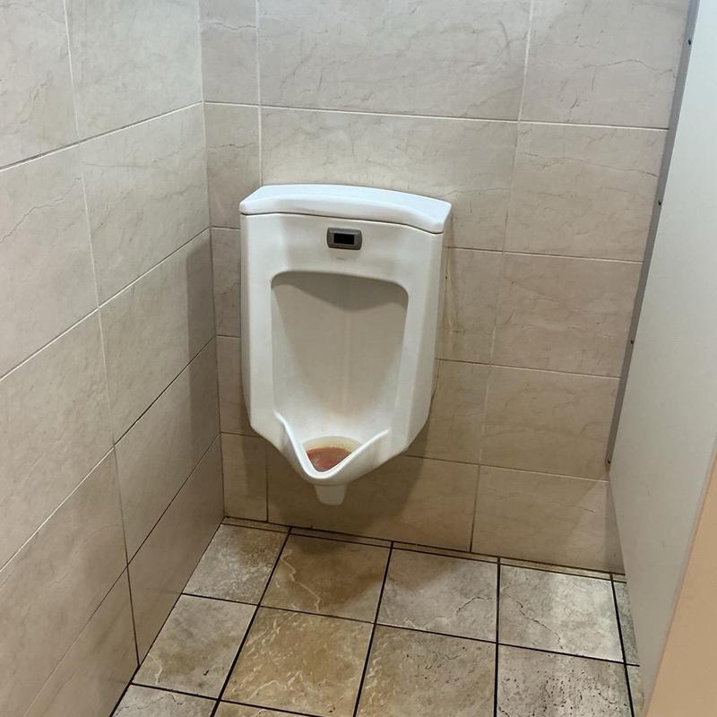 Commercial urinal with water stain in restroom corner