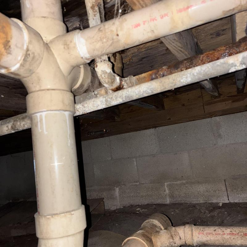 PVC drain pipes and corroded metal plumbing under house crawlspace