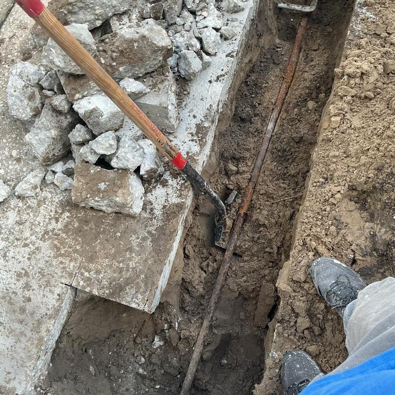 Backflow preventer installation trench with shovel and concrete debris