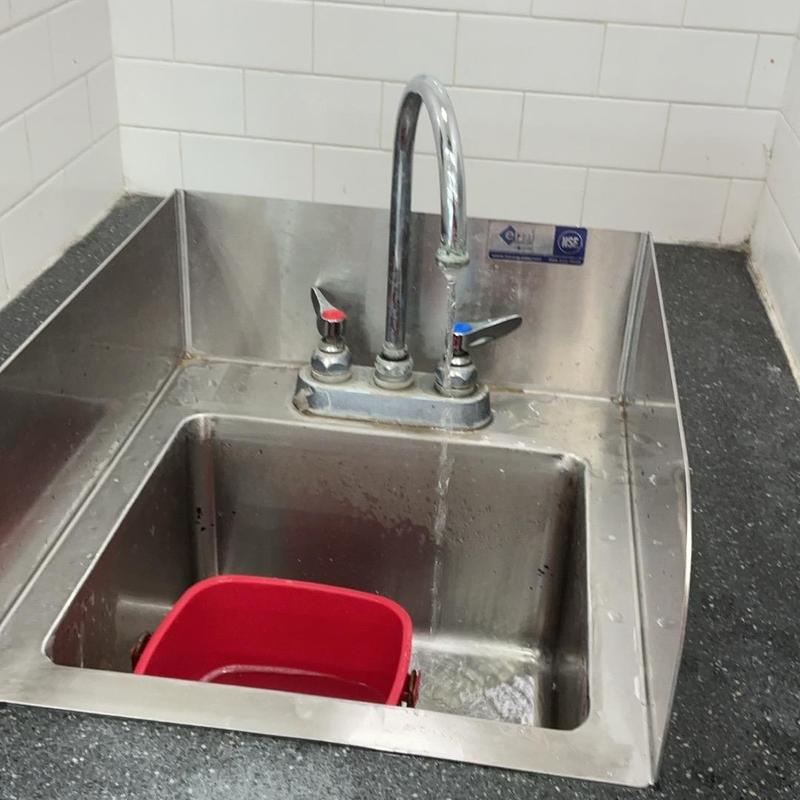 Hand sink faucet with running water and red bucket