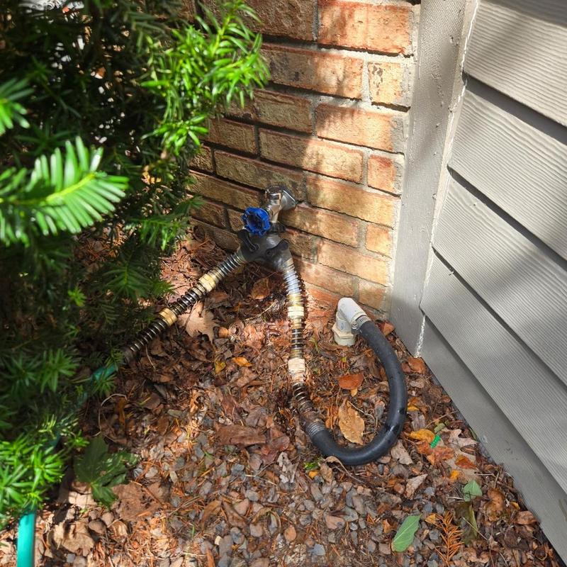 Outdoor spigot with attached garden hoses near brick wall
