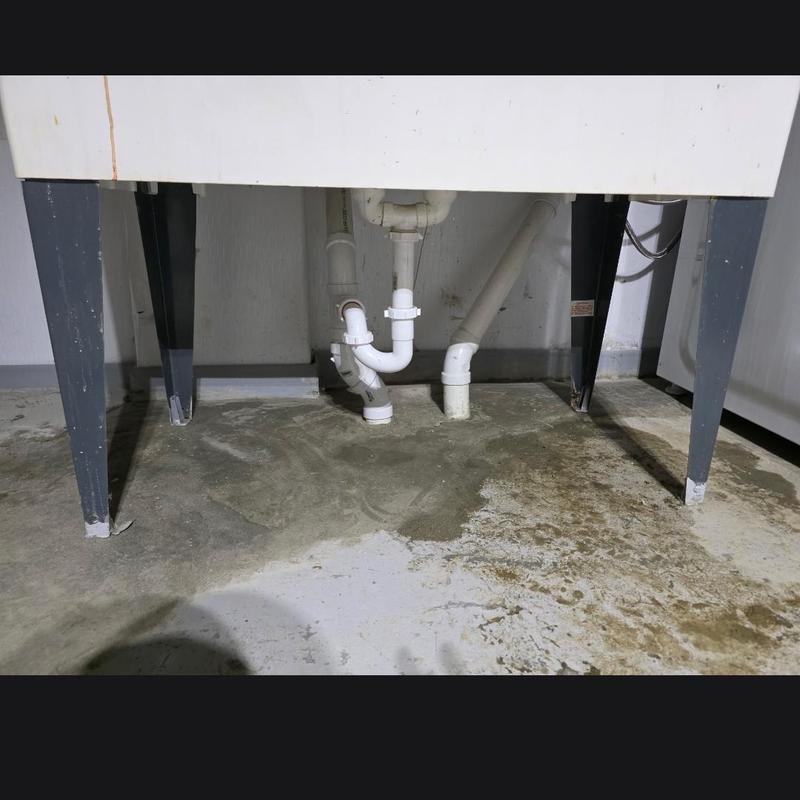 Laundry and kitchen drain pipes under sink with concrete floor