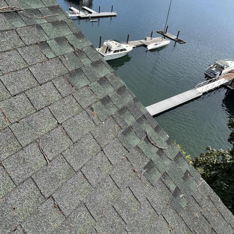Asphalt shingle roof with debris near lakeside dock